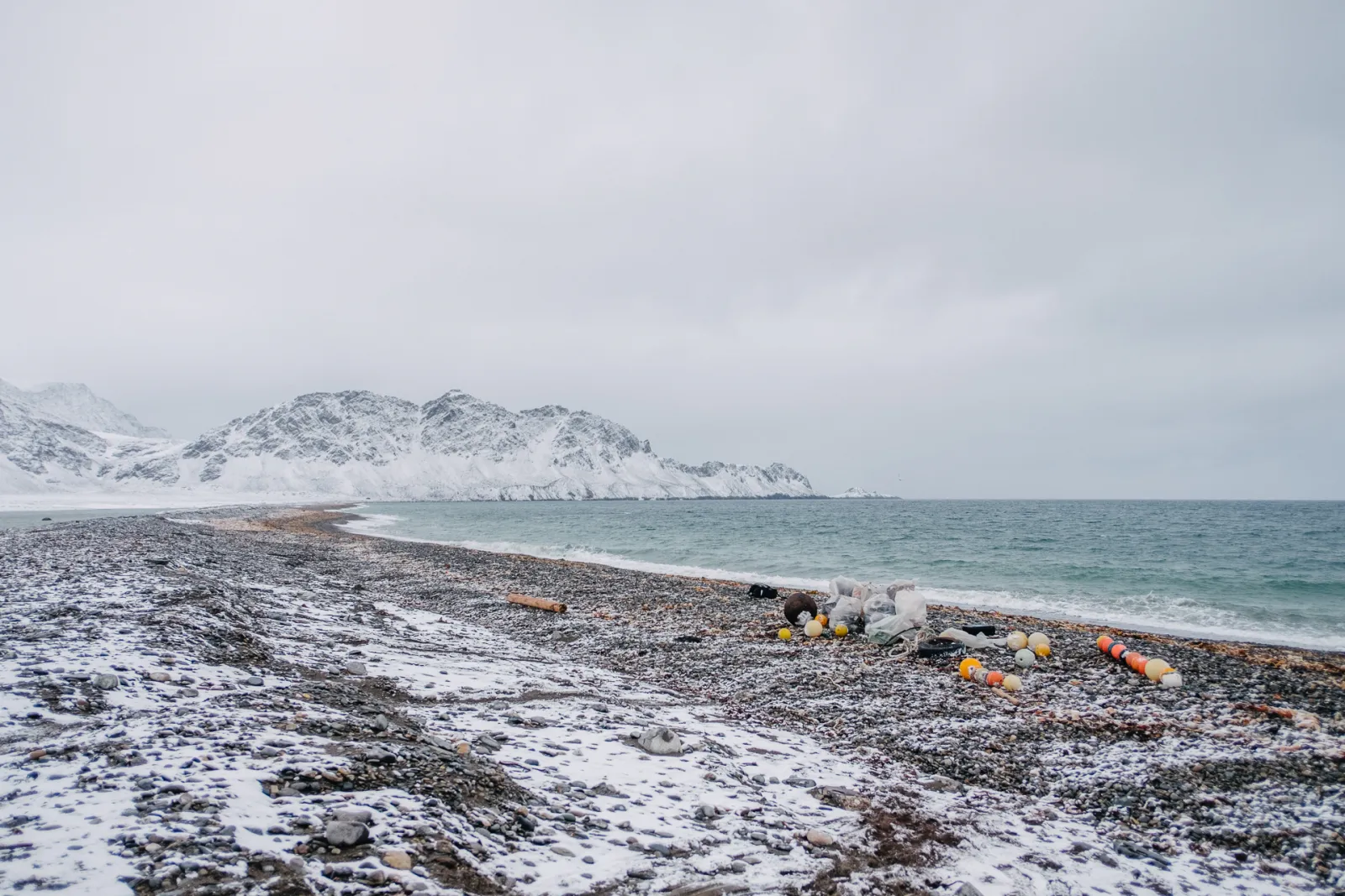 Snødekt strand på Svalbard med innsamlede bøyer og sekker, fjell i bakgrunnen